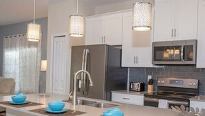 A modern kitchen with white cabinets, stainless steel appliances, and a central island with blue bowls. - Stunning 5 Bd Home w Pool Close to Disney 4822 (Kissimmee)