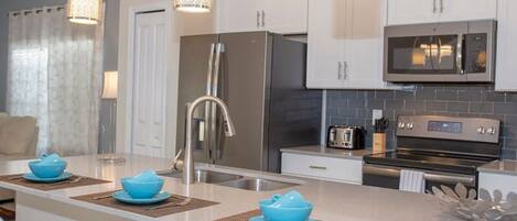 A modern kitchen with white cabinets, stainless steel appliances, and a central island with blue bowls.