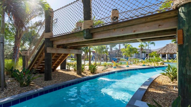 A pool area with a wooden bridge, palm trees, and a clear blue pool. - Marvelous 4Bd w Pool Close to Disney at Storey Lake 2629 (Kissimmee)