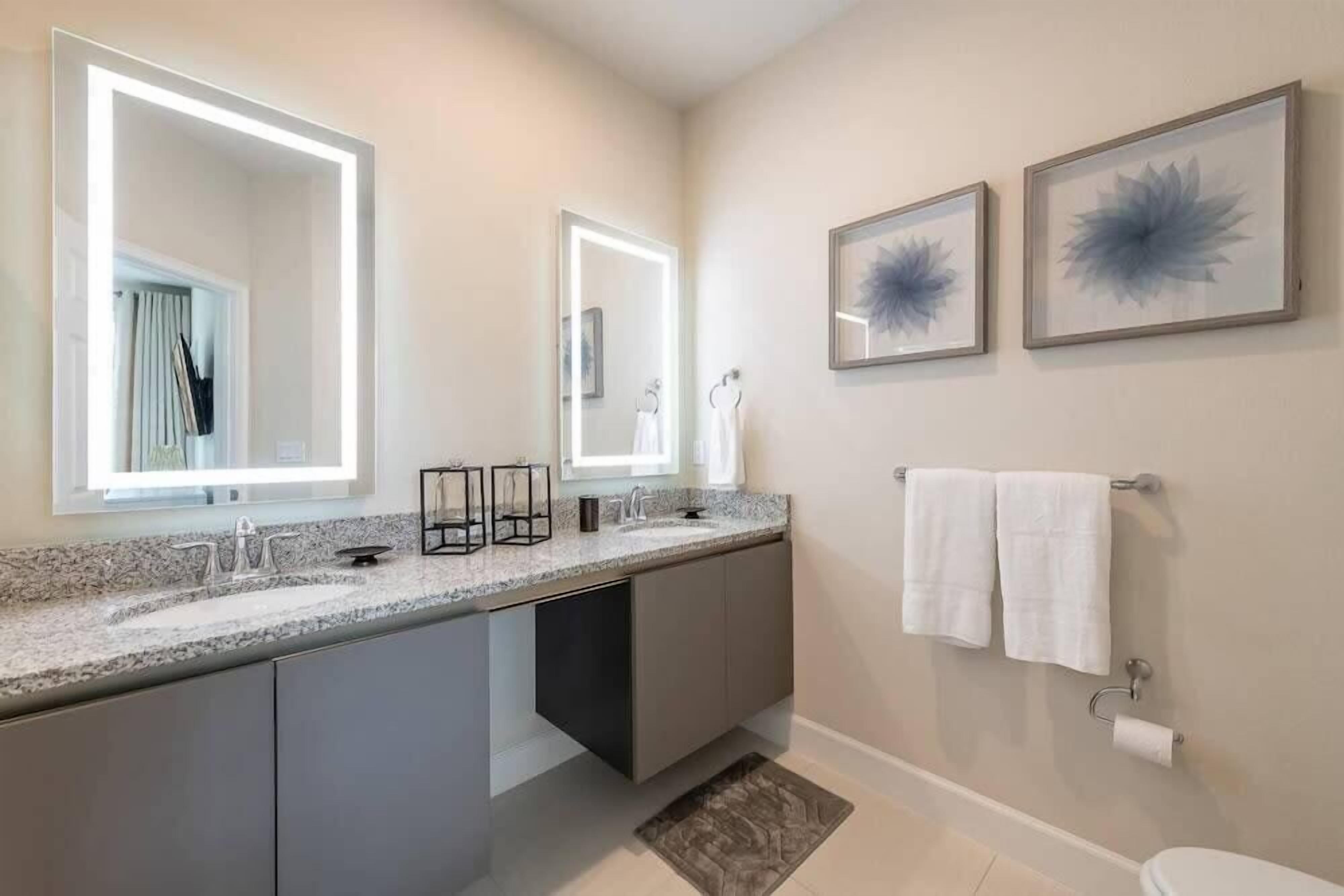 A modern bathroom with a large mirror, two framed artwork, and a toilet with a towel rack.