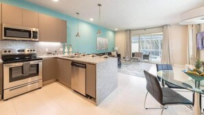 A modern kitchen with stainless steel appliances, a central island, and a dining area with a glass table and chairs. - Marvelous 3Bd w Pool Near Disney at Serenity 1536 (Clermont)