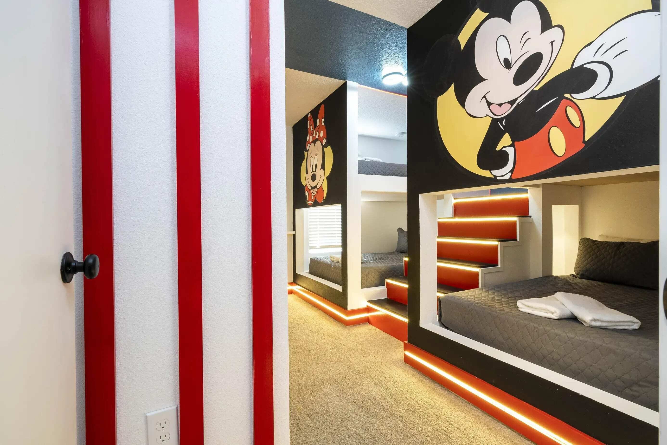 A hotel room with bunk beds, a Mickey Mouse mural, and a red-striped door.