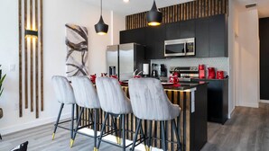 A modern kitchen with a central island, bar stools, a microwave, and a refrigerator.