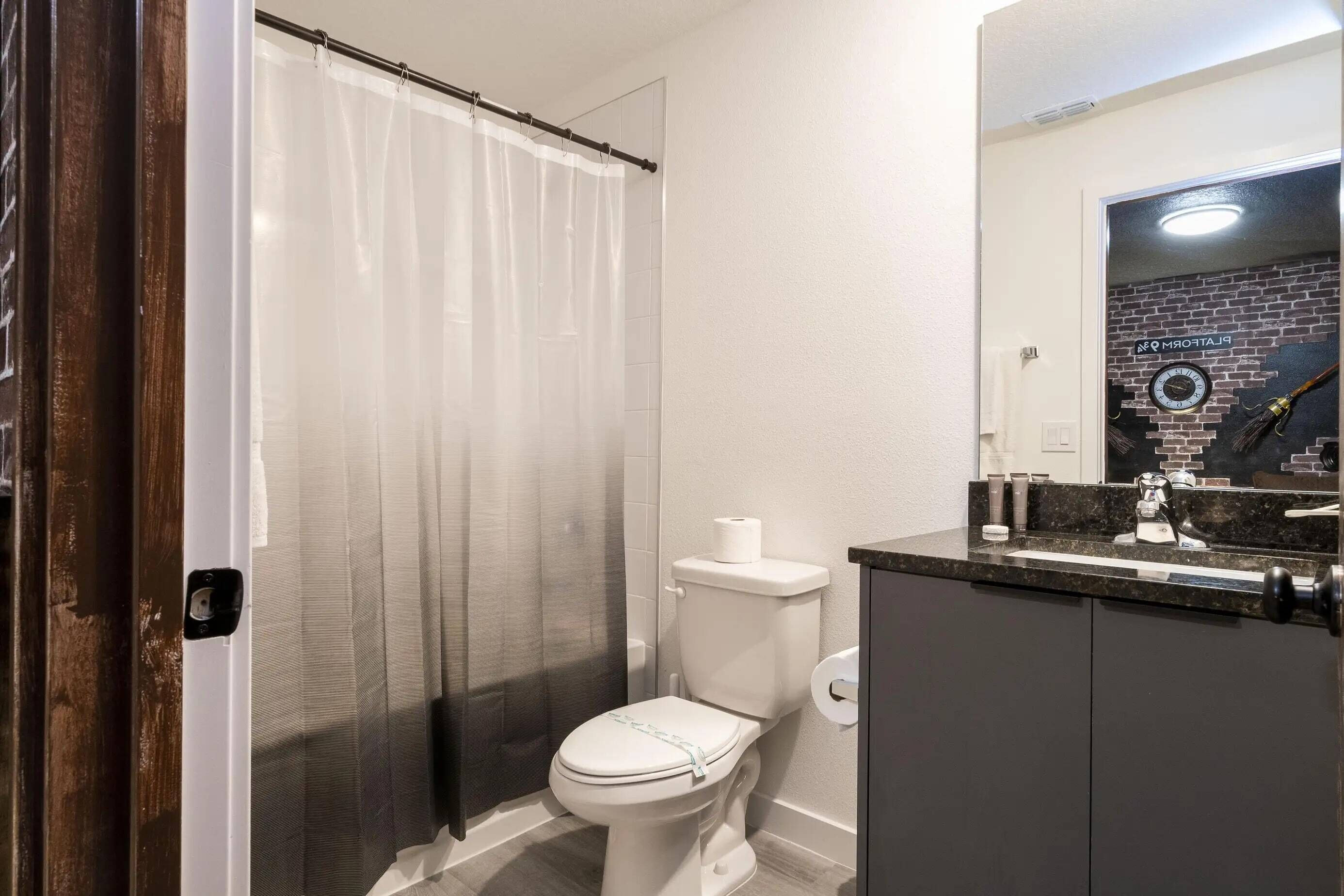 Een badkamer met toilet, douchegordijn, wastafel met spiegel en een handdoekhouder.