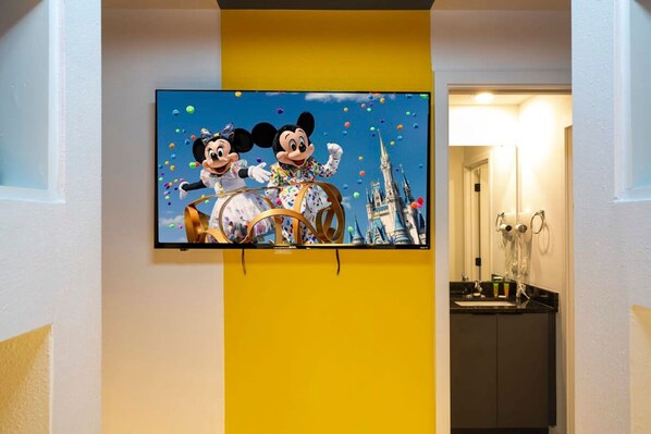 A television mounted on a wall displaying Mickey and Minnie Mouse in a carriage with a castle in the background.