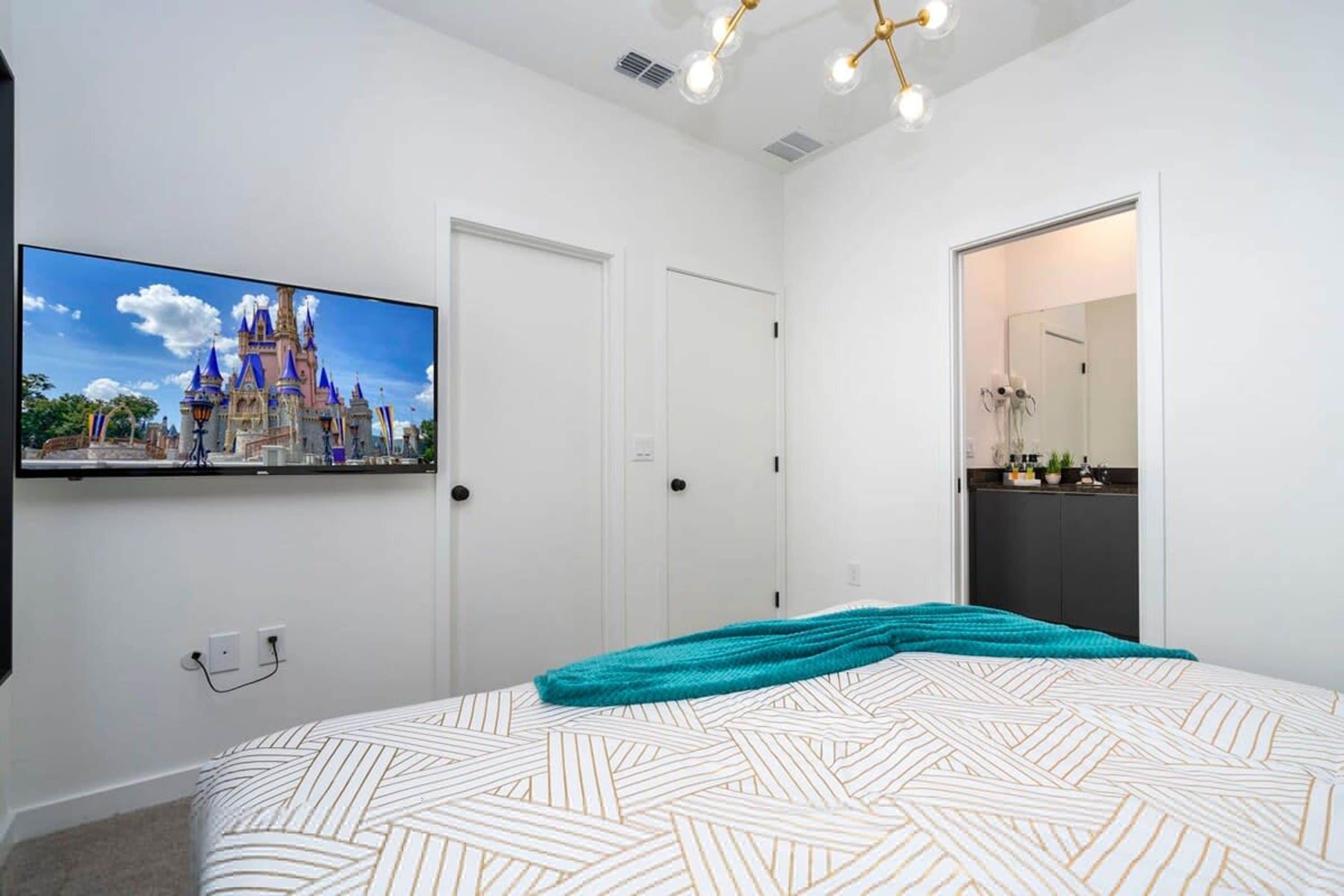 Een slaapkamer met een bed, een televisiescherm waarop een kasteel te zien is, witte deuren en een zichtbare badkamer door een open deur.