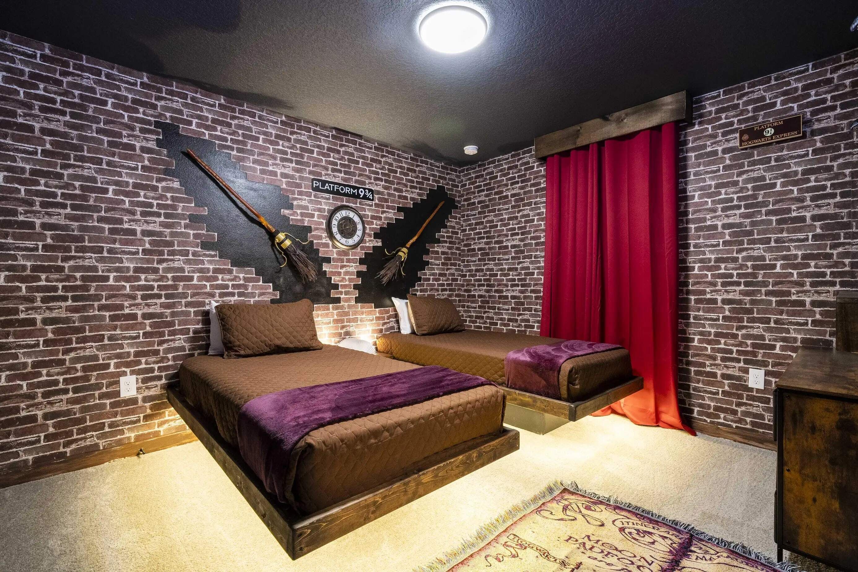 A room with a brick wall, a bed with a purple blanket, a small table, and a red curtain.