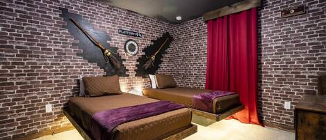 A room with a brick wall, a bed with a purple blanket, a small table, and a red curtain.