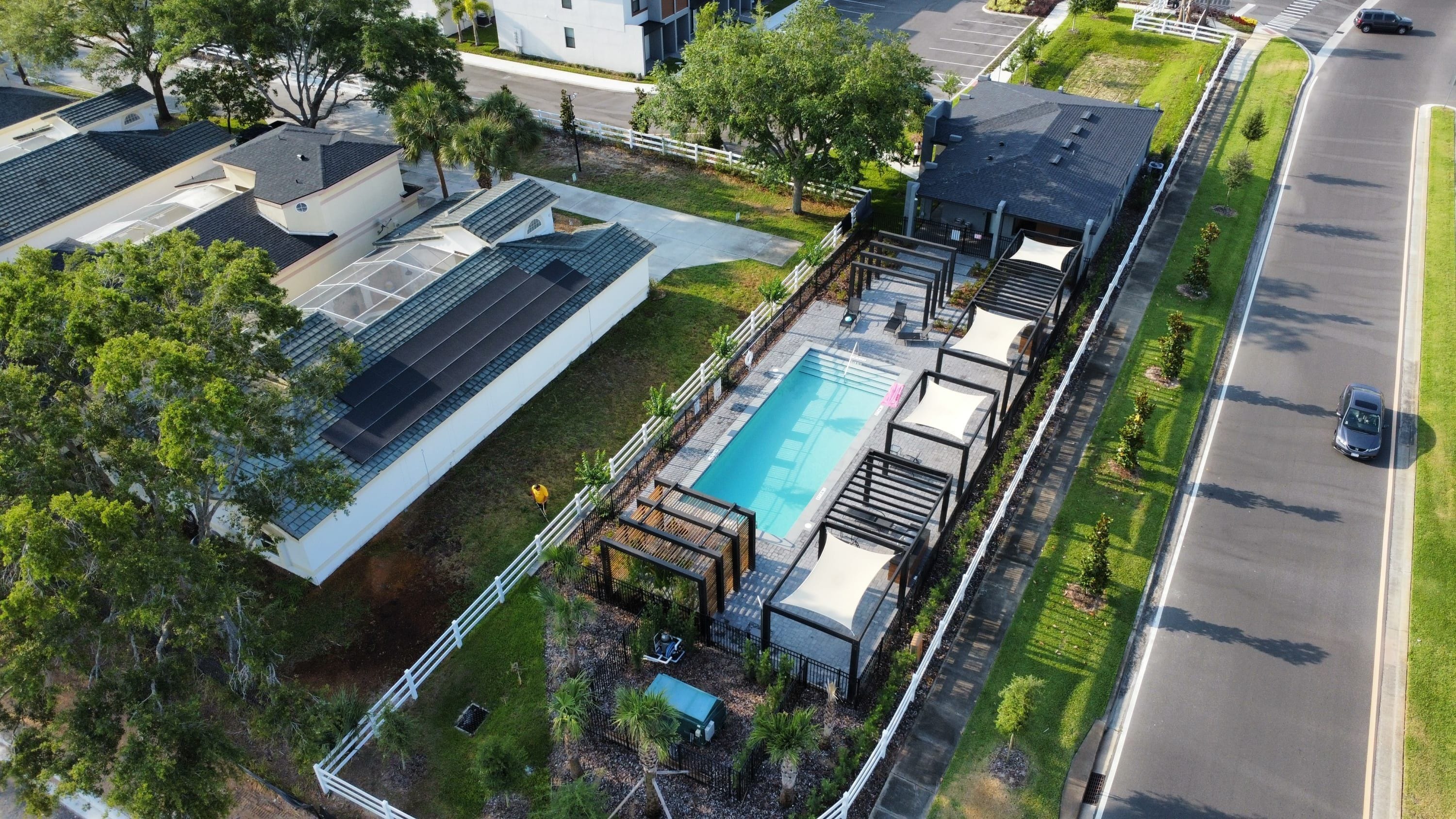 An aerial view of a residential area with a swimming pool, solar panels, and a road.