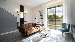 A modern living room with a brown leather sofa, a round mirror, and a teal armchair.