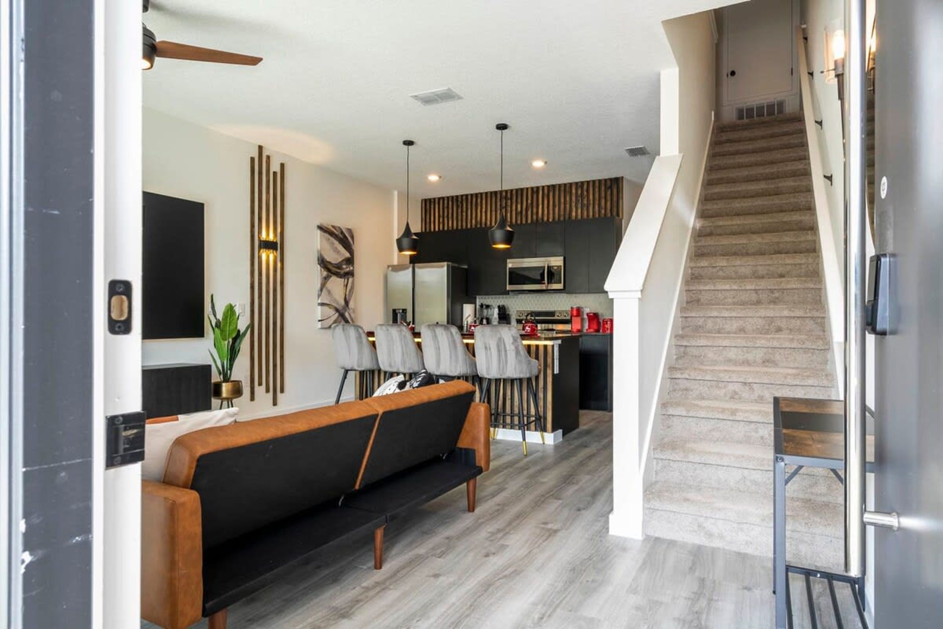Una sala moderna con un sofá, un comedor con sillas, una cocina con microondas y una escalera.