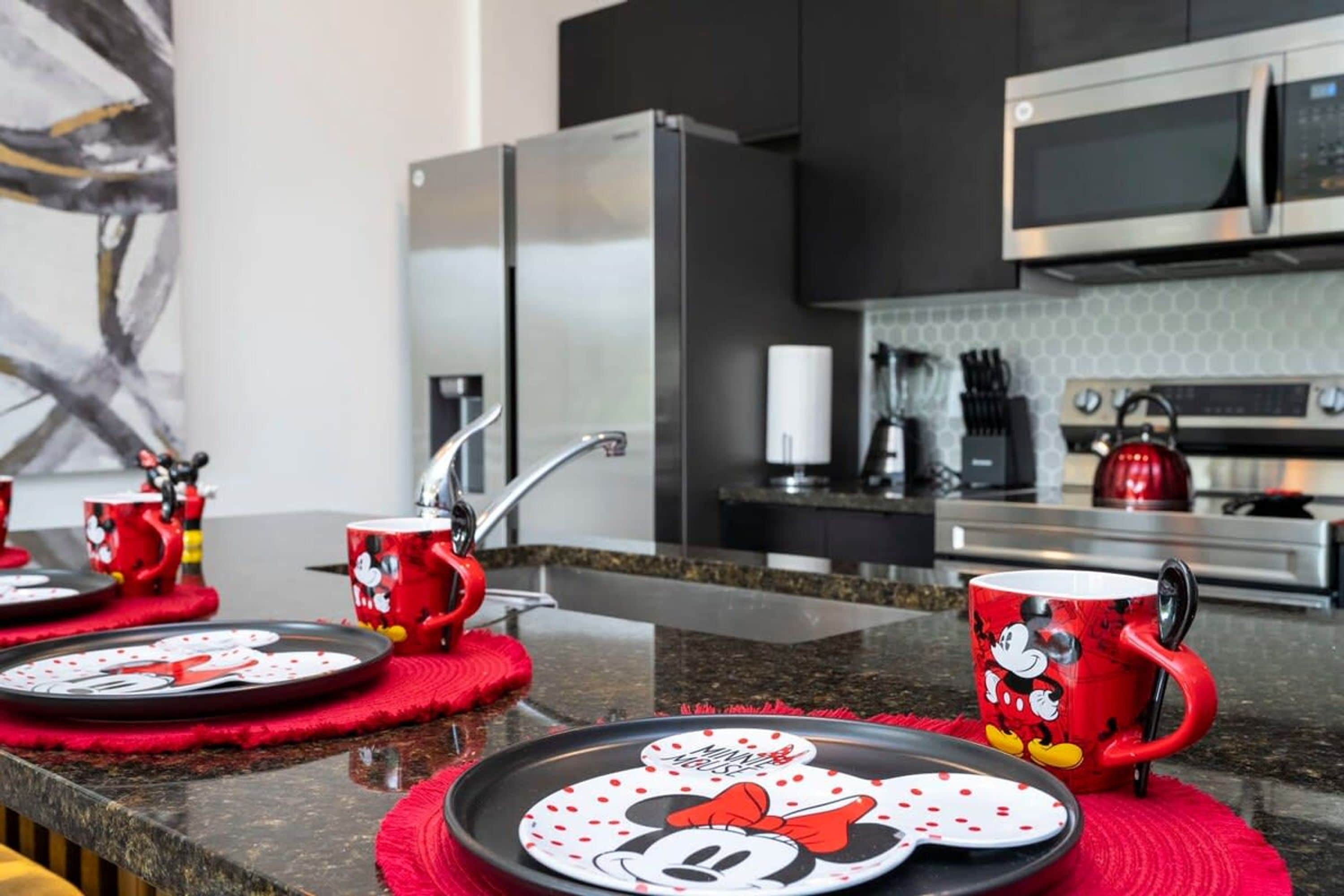 A modern kitchen with stainless steel appliances, red Minnie Mouse mugs, and plates on the counter.