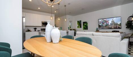 A modern living room with a wooden dining table, teal chairs, and a white sofa.