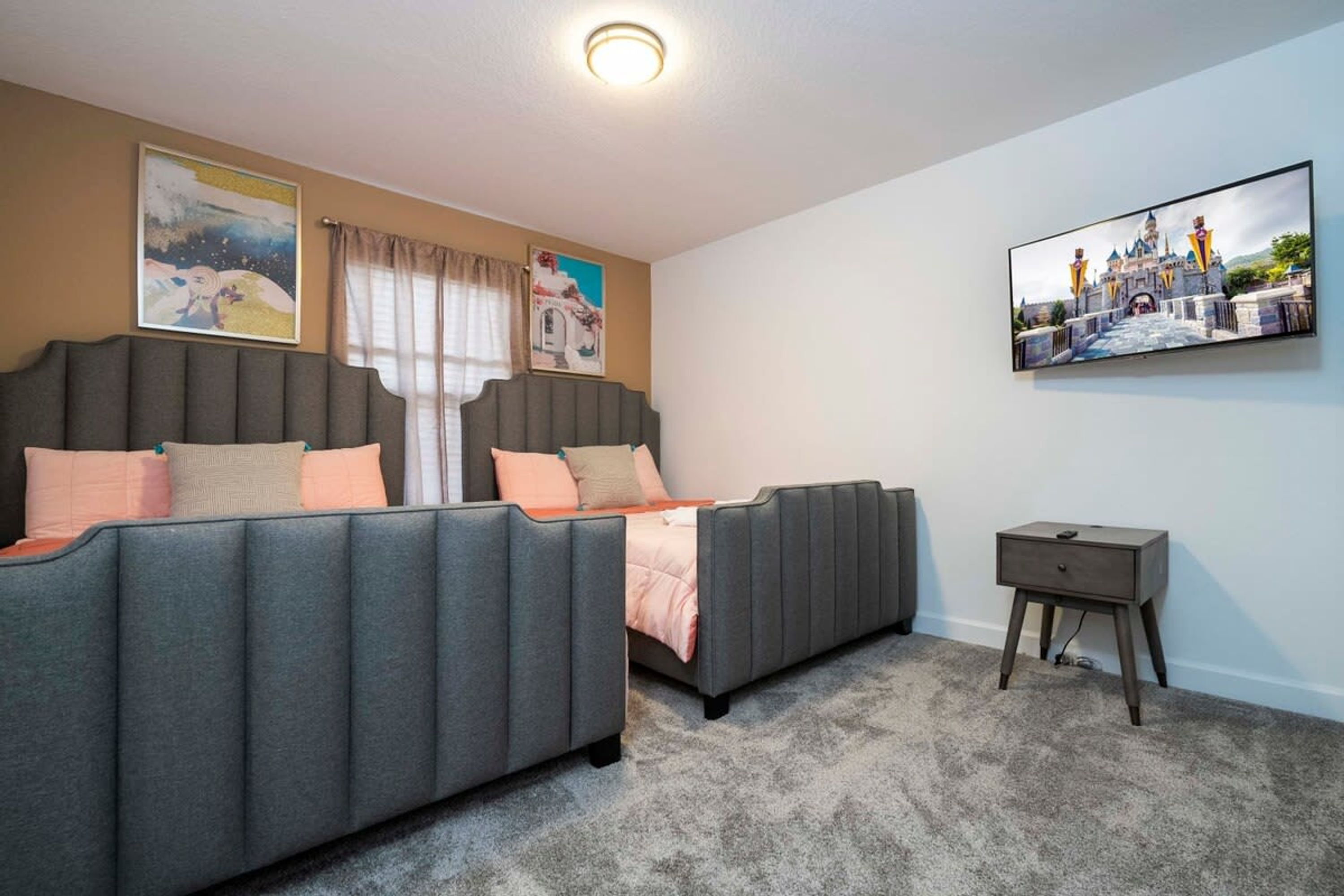 A bedroom with two beds, a bedside table, and a TV on the wall.