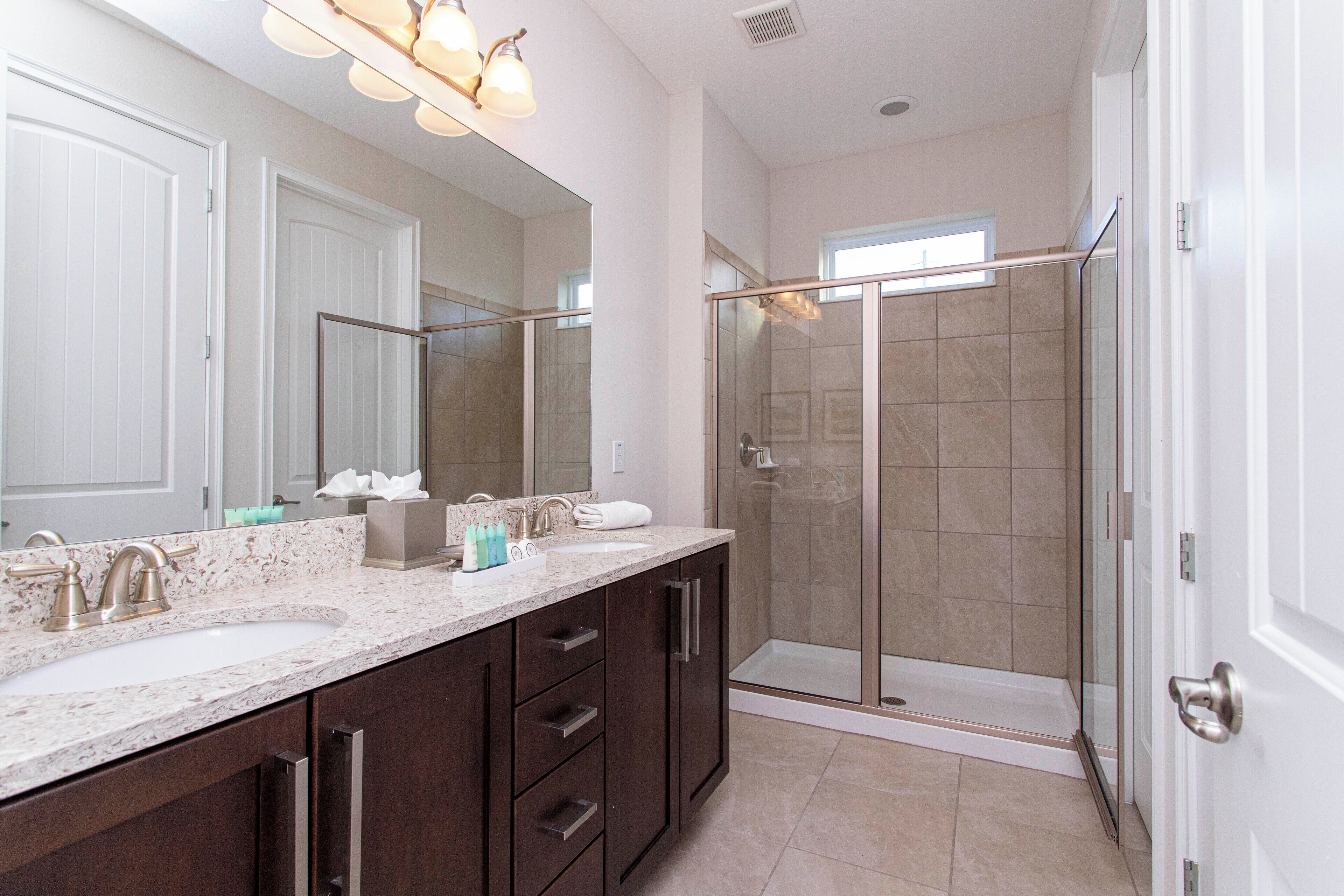 A modern bathroom with two sinks, a large mirror, and a glass-enclosed shower.
