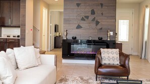 Una sala de estar moderna con chimenea, un sofá, un sillón de cuero y una cocina al fondo.