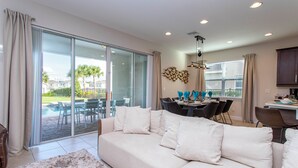 Amplia sala de estar con un sofá grande, una zona de comedor con sillas y vista a una piscina a través de puertas de vidrio.
