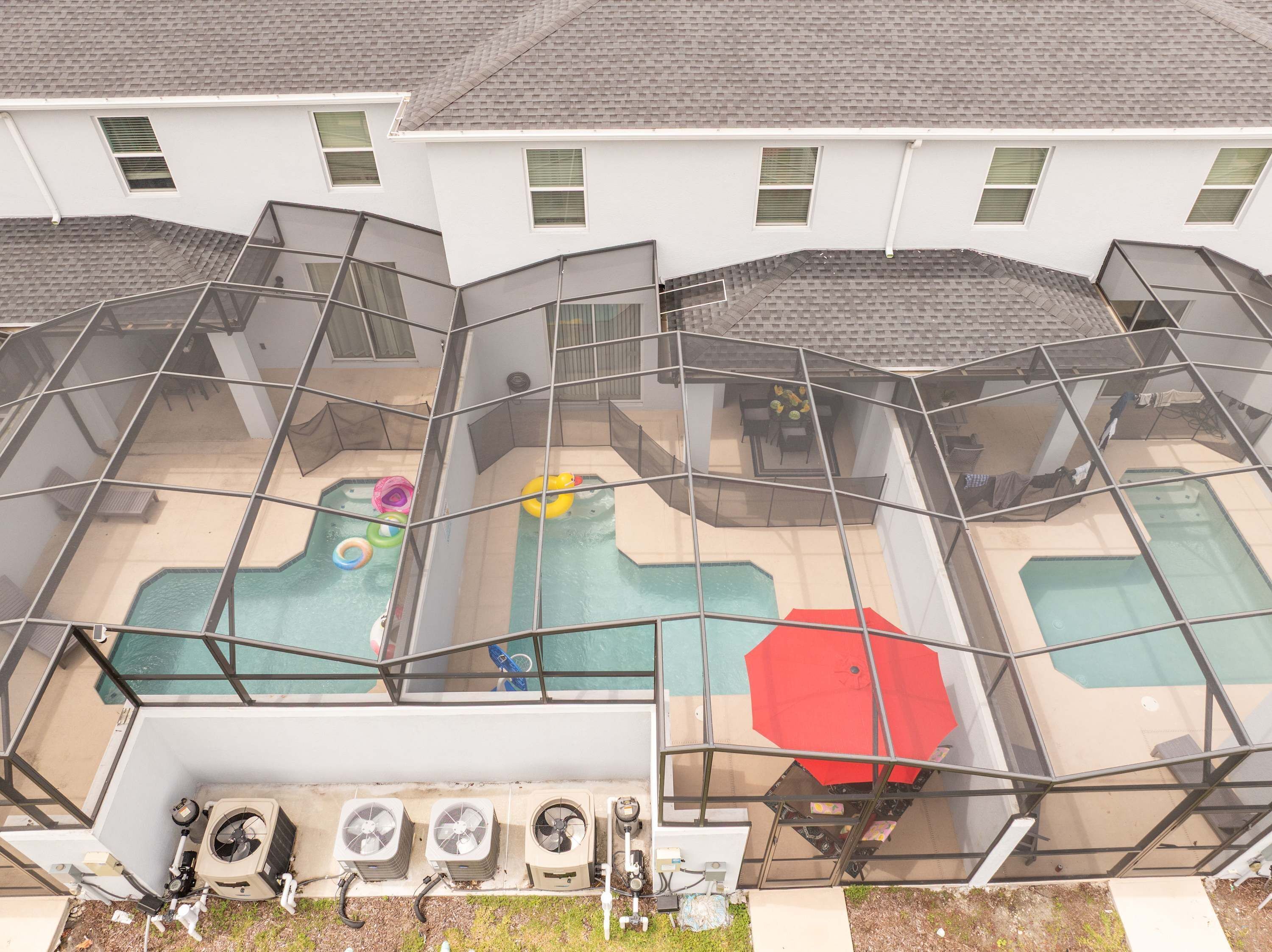 Un edificio residencial con piscina exterior cubierta, unidades de aire acondicionado y un paraguas rojo.