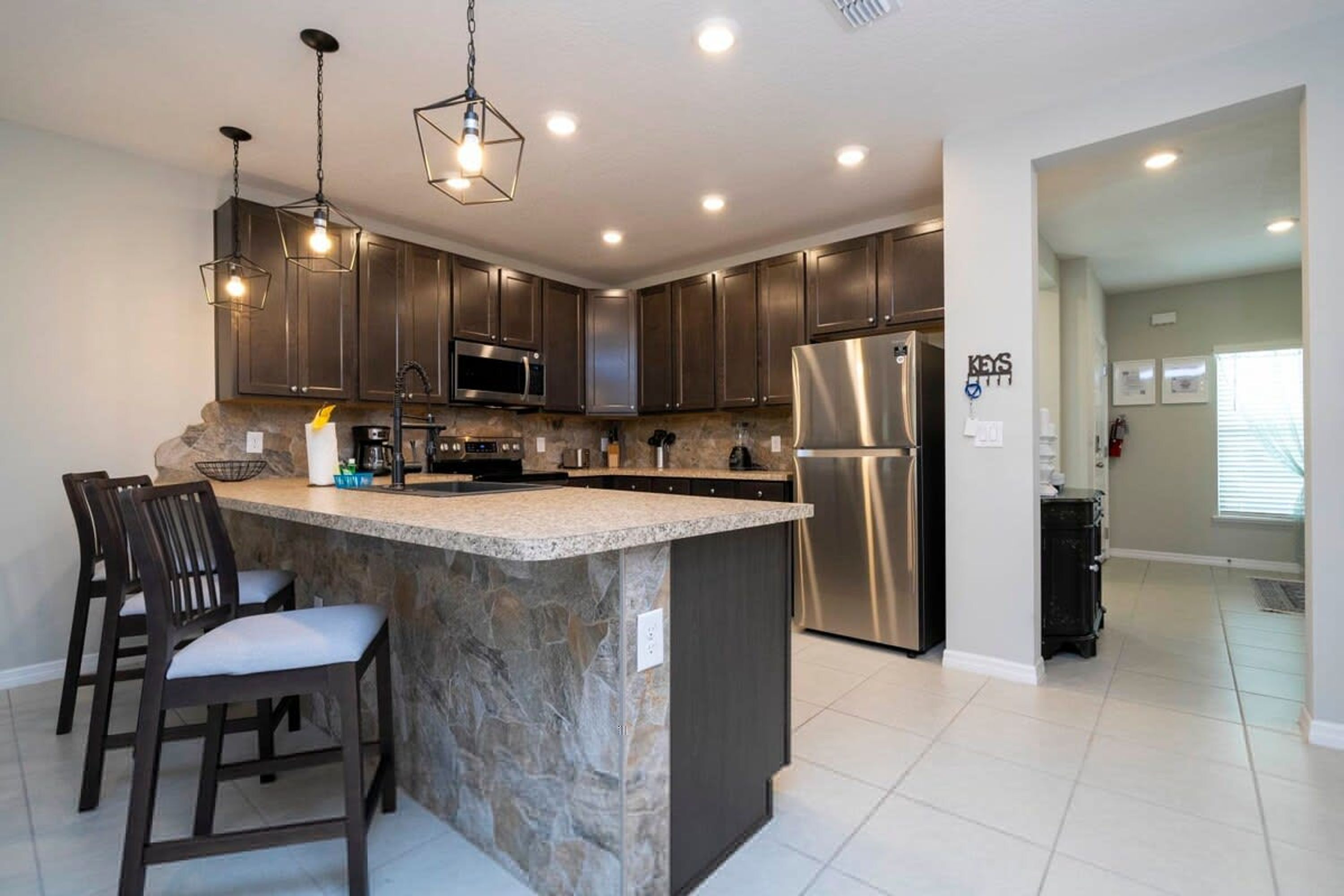 A modern kitchen with dark cabinets, stainless steel appliances, and a central island with bar stools.