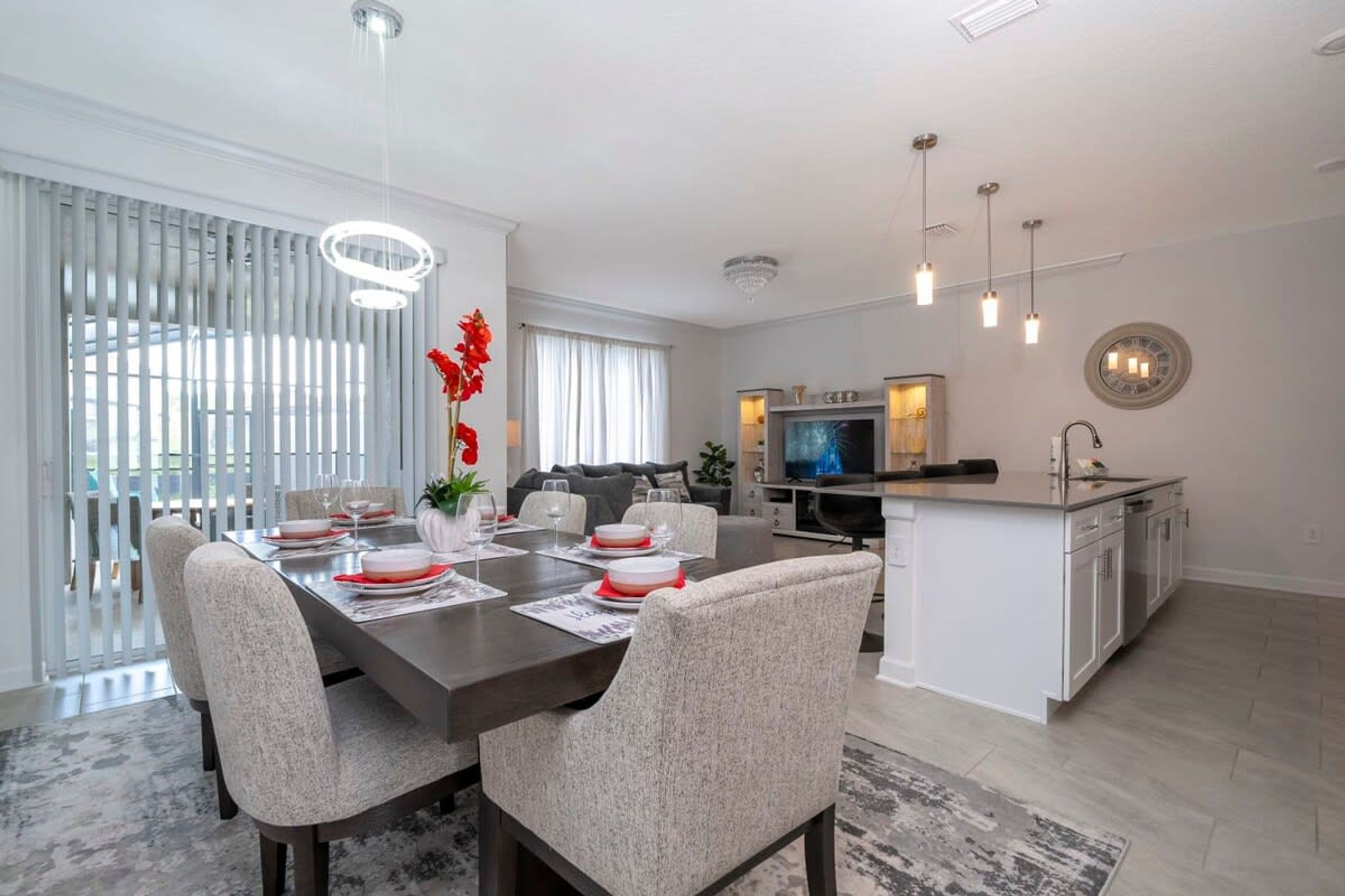 A modern kitchen with a central island, white cabinetry, and a dining area with a dark wooden table and light grey upholstered chairs.