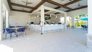 A spacious outdoor dining area with white chairs and tables, ceiling fans, and a bar area with a TV screen. - Gorgeous 4Bd With Pool at Storey Lake Resort 4475 (Kissimmee)