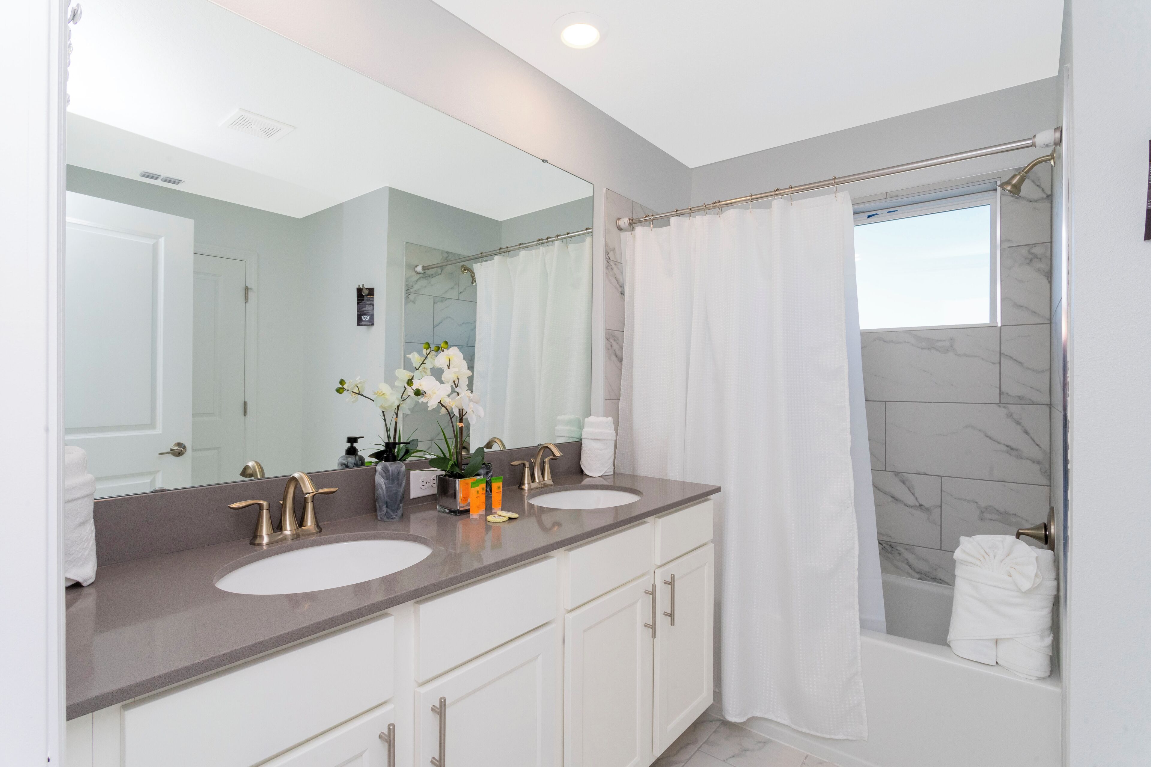 A modern bathroom with two sinks, a large mirror, and a shower area.
