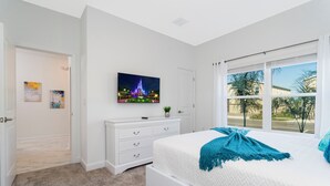 Een slaapkamer met een bed, een kaptafel, een televisie aan de muur en een raam met uitzicht op palmbomen.