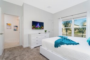 A bedroom with a bed, a dresser, a TV on the wall, and a window with a view of palm trees. - Stunning 4 Bd w Pool Close to Disney Champions Gate 990 (Davenport)