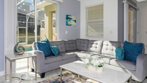 A modern living room with a grey sectional sofa, a white coffee table, and a glass door leading to a balcony. - Stunning 4 Bd w Pool Close to Disney Champions Gate 990 (Davenport)