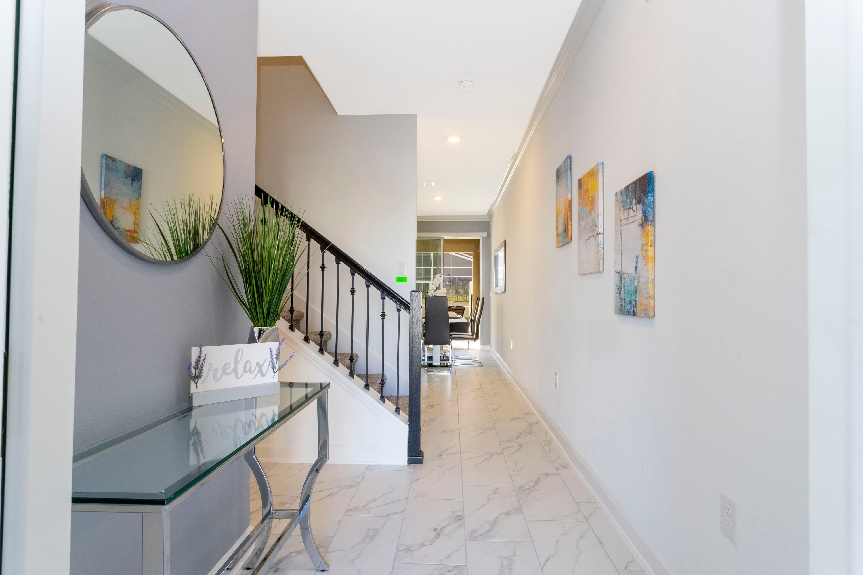 A modern hallway with a glass desk, a mirror, and a staircase.