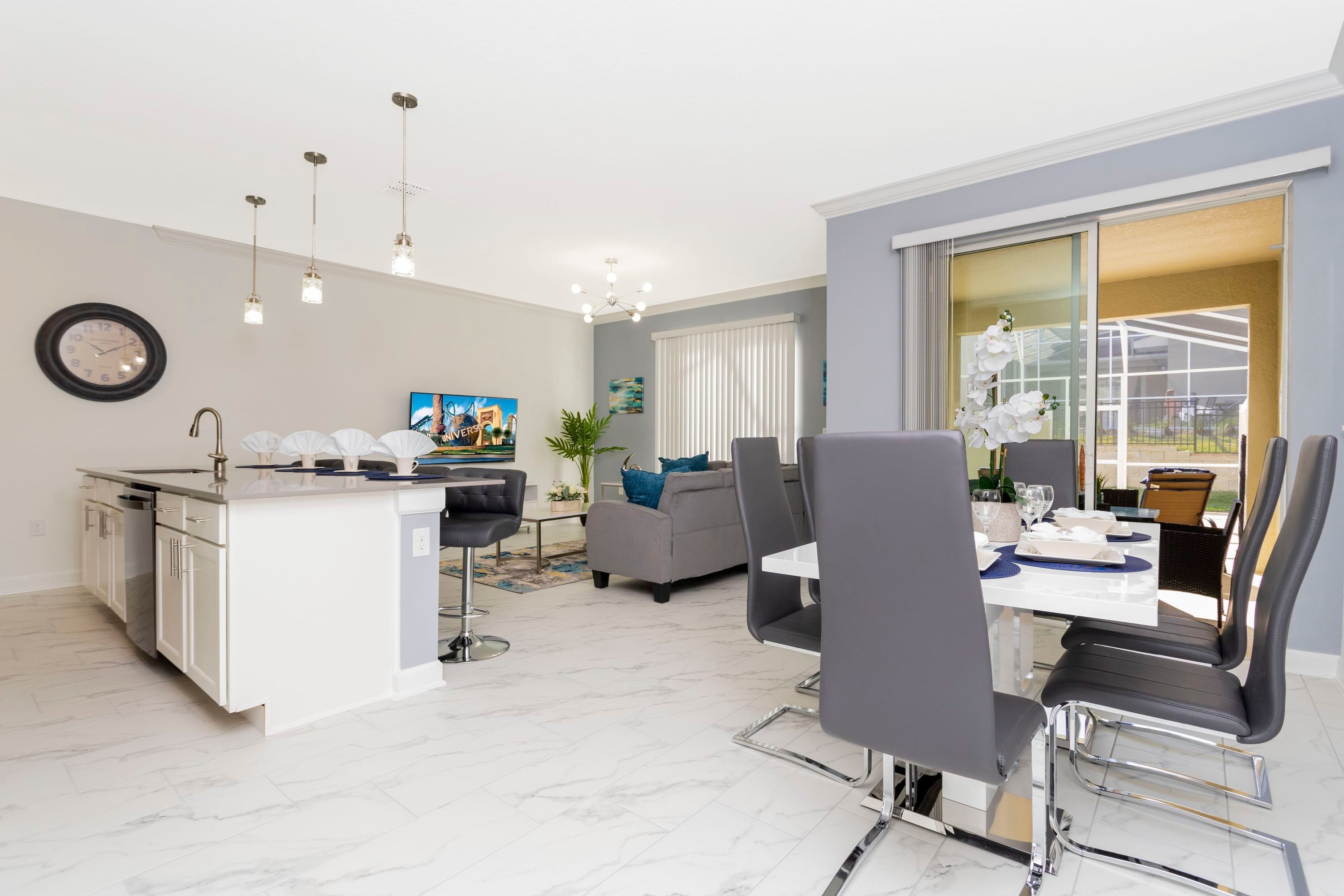 Una cocina moderna con una isla central, un comedor con mesa y sillas, y una sala de estar con sofá y una planta.