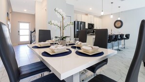 A modern dining area with a white table set for four, black chairs, and a decorative orchid plant. - Stunning 4 Bd w Pool Close to Disney Champions Gate 990 (Davenport)