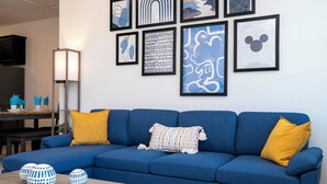A blue sofa with yellow cushions, a coffee table with decorative vases, and a wall with framed artwork. - Splendid 4Bd Close to Disney Holly Village 132 (Davenport)