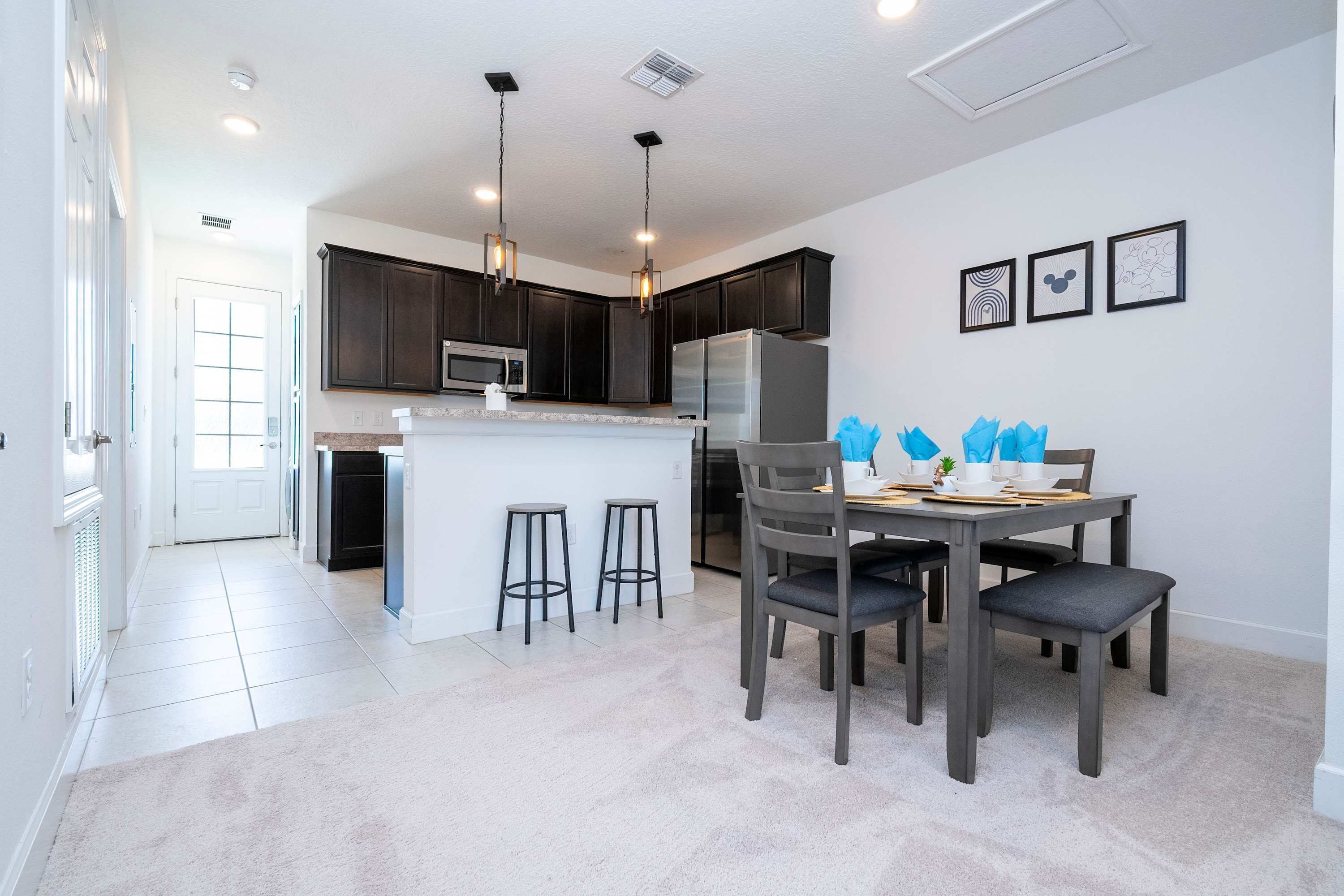 A modern kitchen with dark cabinets, a central island, bar stools, and a dining table set for four.