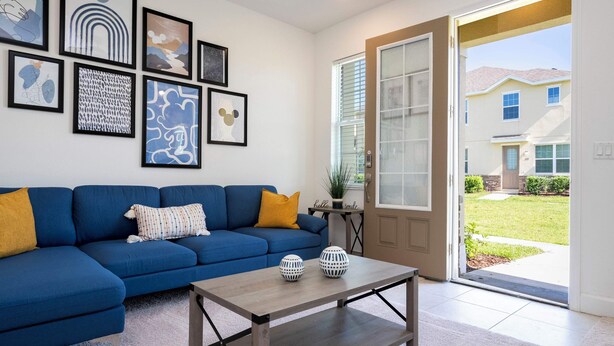 A living room with a blue sectional sofa, a coffee table, and various framed artworks on the wall. - Splendid 4Bd Close to Disney Holly Village 132 (Davenport)