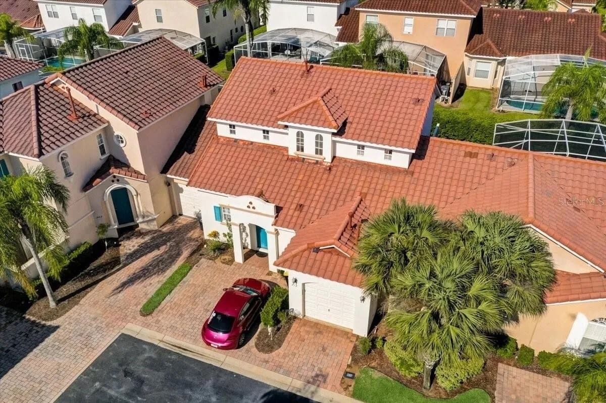 A residential area with houses, a red car parked in the driveway, and a palm tree.