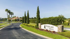En skylt med texten ”Tuscan Hills” som markerar infarten, vilken är vackert anlagd med palmer och en svängd väg.