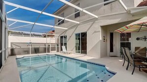 En swimmingpool med ett takförsett uteområde, utomhusmöbler och fri sikt mot himlen.
