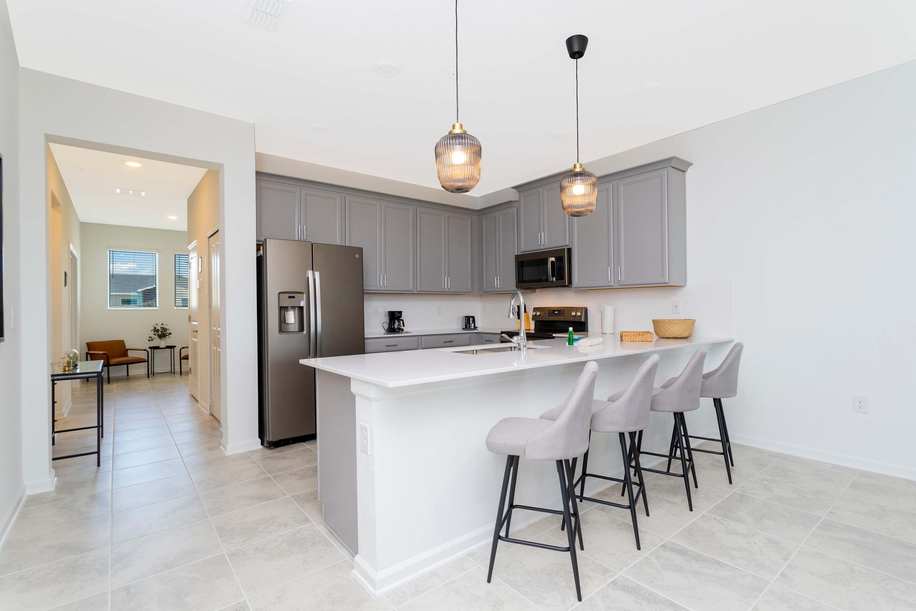 A modern kitchen with grey cabinets, a stainless steel refrigerator, a microwave, and a white island with bar stools.