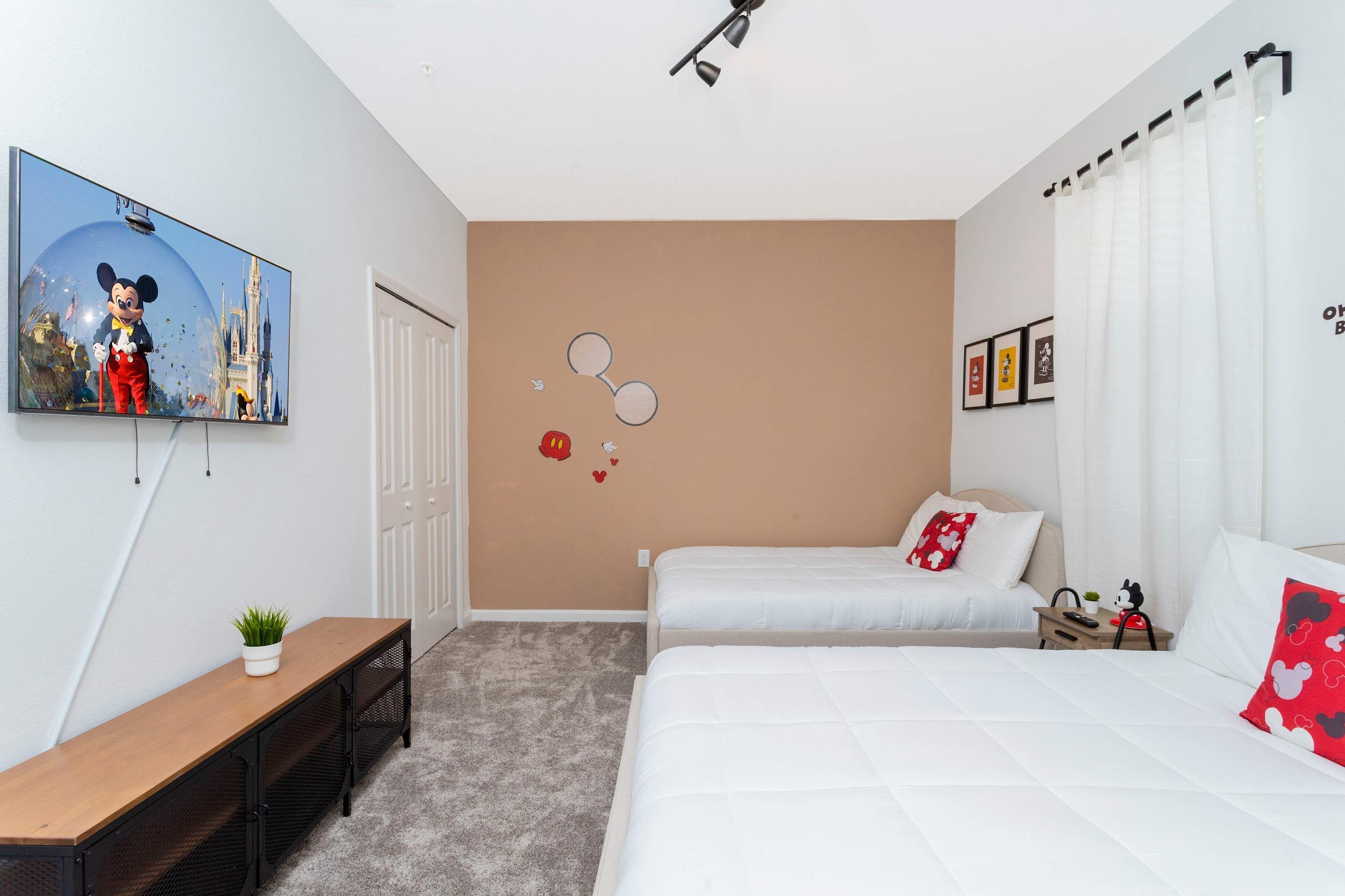 A hotel room with a bed, a desk, a TV, a bench, and a wall with Mickey Mouse-themed decorations.