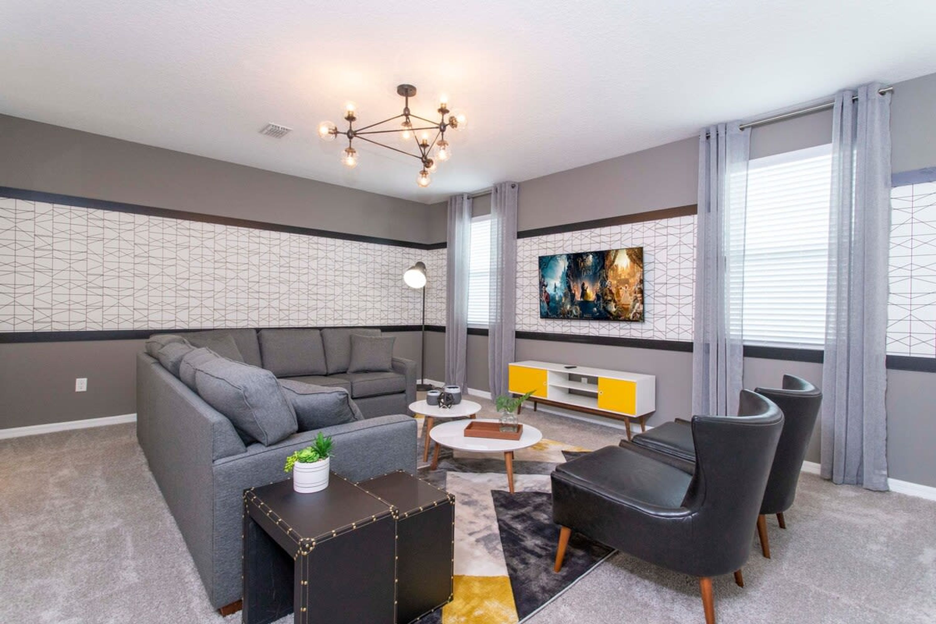 A modern living room with a grey sofa, black armchairs, a coffee table, and a TV on the wall.