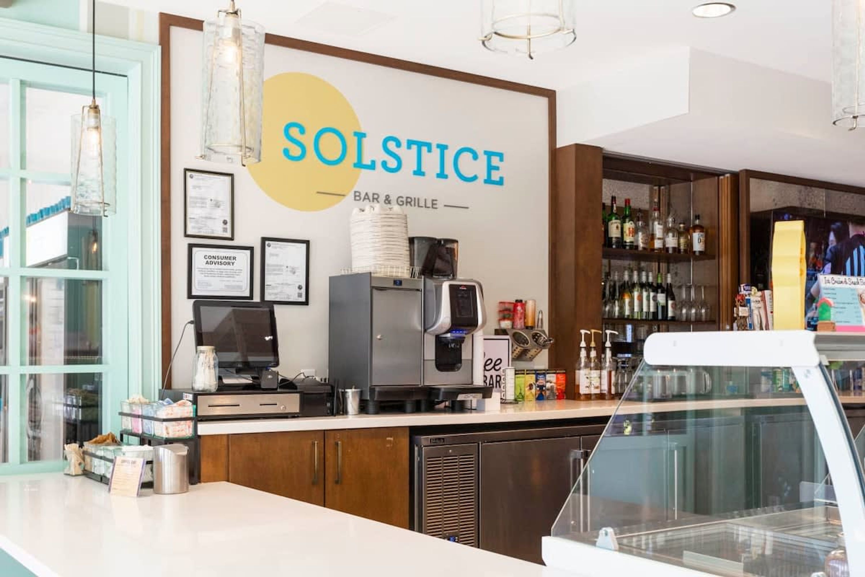 L’intérieur d’un bar-restaurant, avec un comptoir, une machine à café et des étagères remplies de bouteilles.