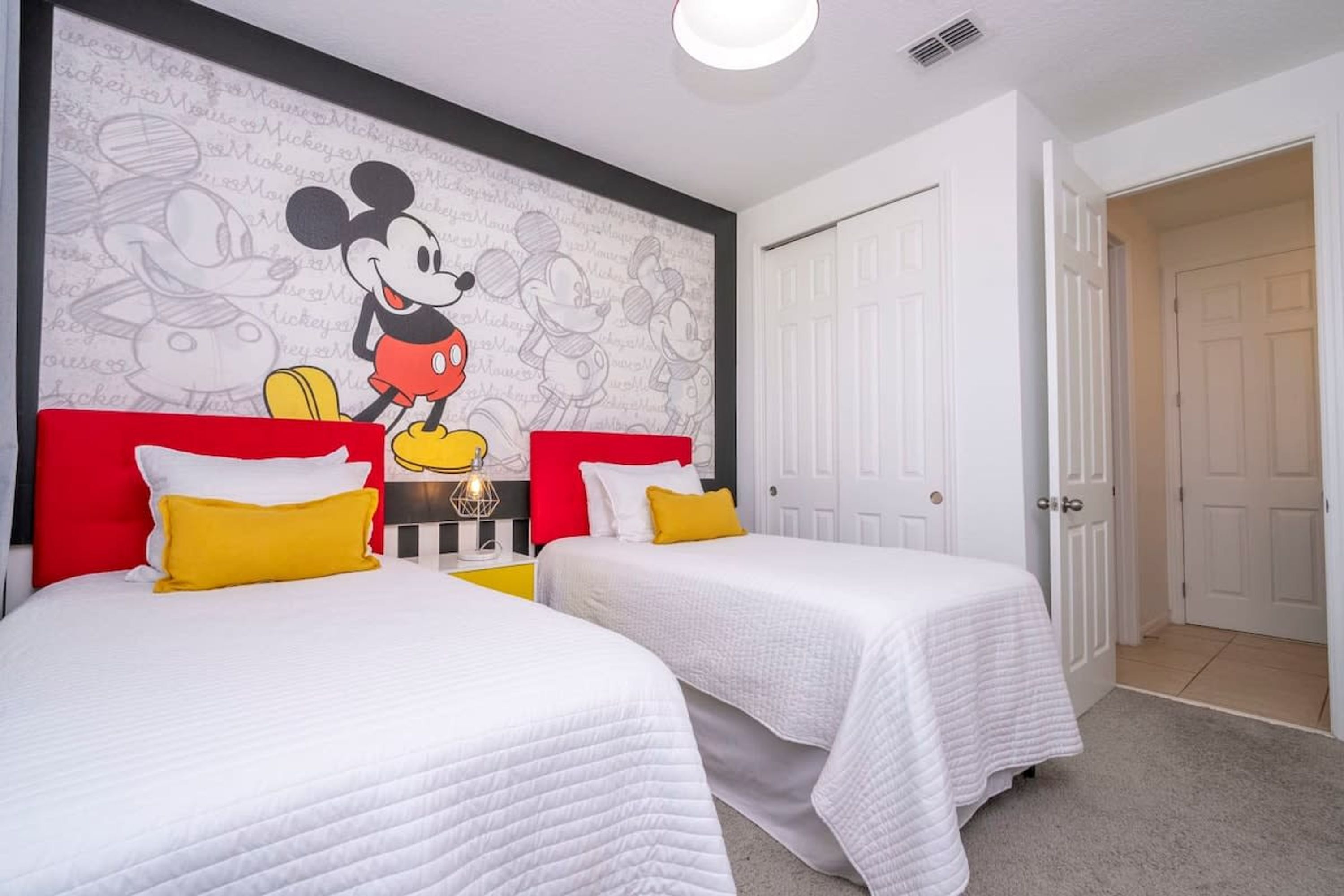 A hotel room with two beds, each with white bedding and red headboards. There is a Mickey Mouse mural on the wall above the beds.