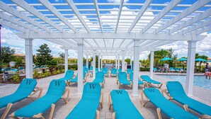 A covered pool area with rows of turquoise lounge chairs and a pool in the background. - Splendid 5 Bd w Screened Pateo Pool Windsor Westside 8921 (Kissimmee)