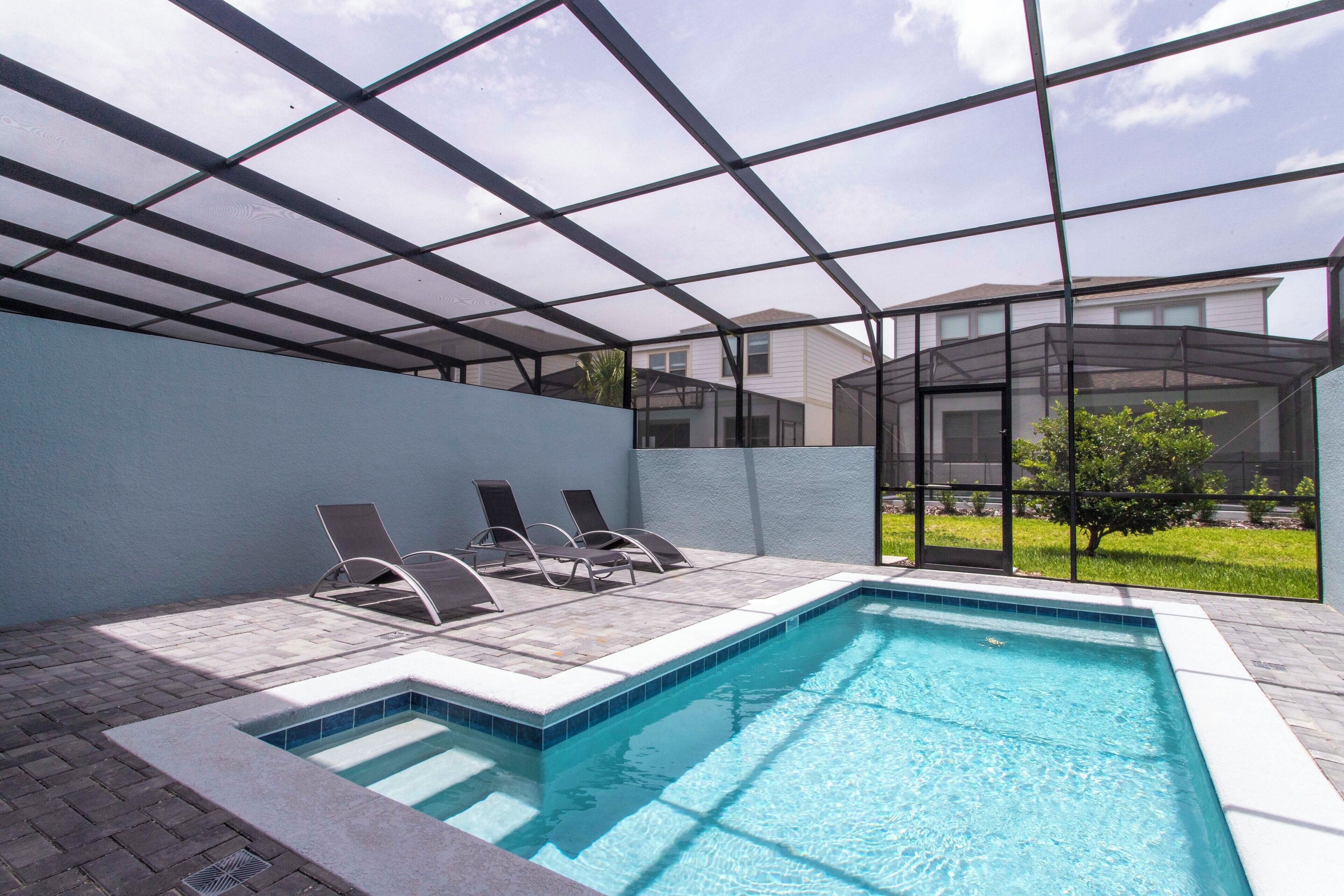 En swimmingpool med et glasindhegning, liggestole og et hus i baggrunden.