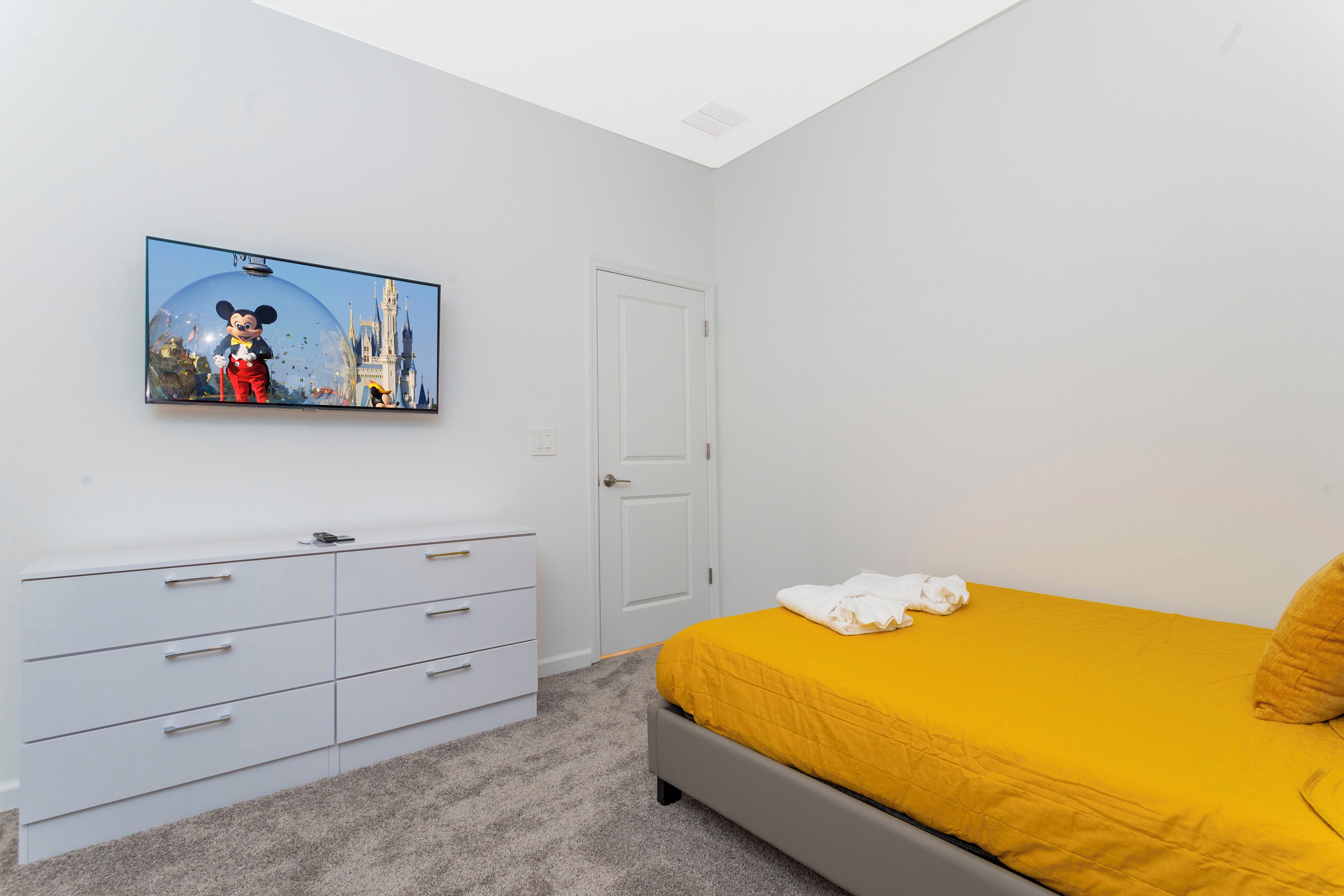 A bedroom with a bed, a white dresser, a television displaying a cartoon character, and a door.