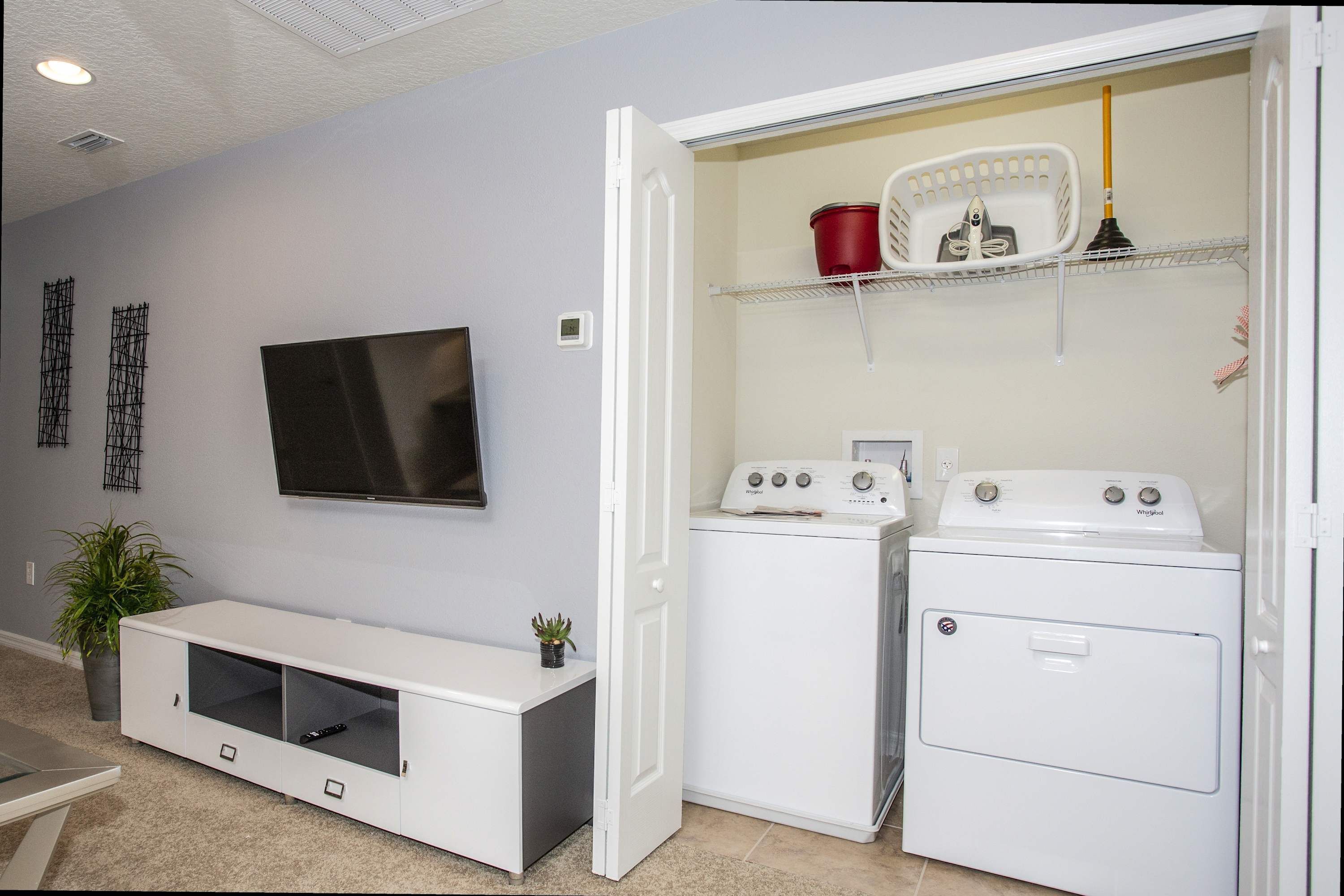 Un cuarto de lavado con lavadora y secadora, un televisor y un espacio de almacenamiento.