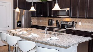 Una cocina moderna con gabinetes de madera oscura, electrodomésticos de acero inoxidable, encimeras de granito e iluminación colgante.
