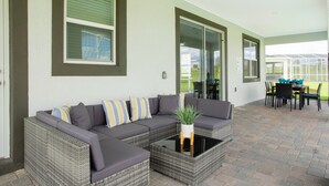 A covered patio area with a sectional sofa, a glass-top coffee table, and a dining table with chairs. - Joyful 8Bd Single Family w Pool Champions Gate 9262 (Davenport)