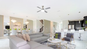 A modern living room with a grey sectional sofa, a round coffee table, and a chandelier. - Joyful 8Bd Single Family w Pool Champions Gate 9262 (Davenport)